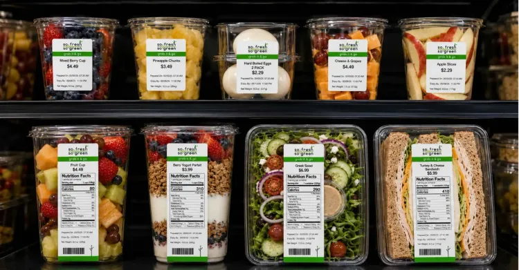 Fresh grab-and-go food items in a refrigerated display cooler with clear printed labels for prepared dates, use-by times, nutrition facts, and product information.