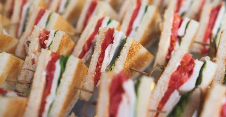 Rows of toasted chicken, tomato, and leafy green sandwiches prepared for a large catering order.