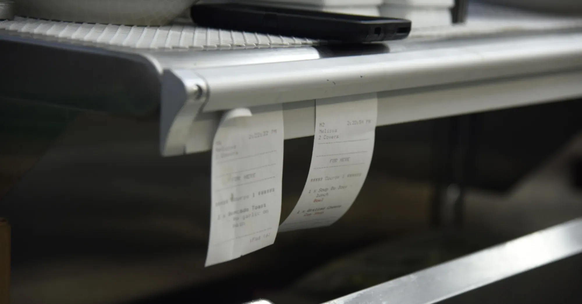 Paper tickets hanging in a restaurant back-of-house area, showing manual foodservice workflows that can become harder to manage under operational pressure.