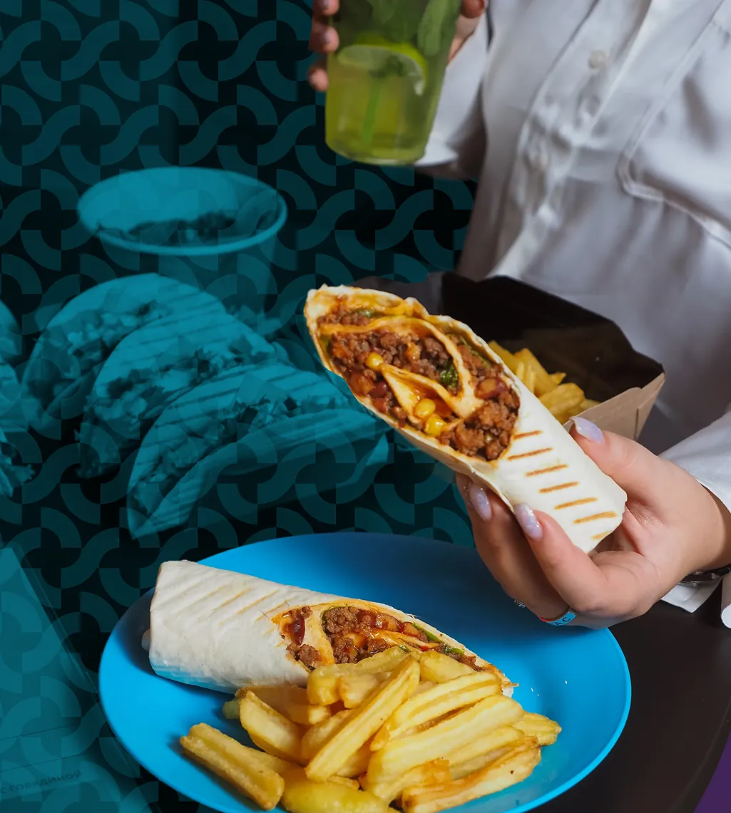 A hand holding a freshly grilled quick-service wrap over a plate of fries