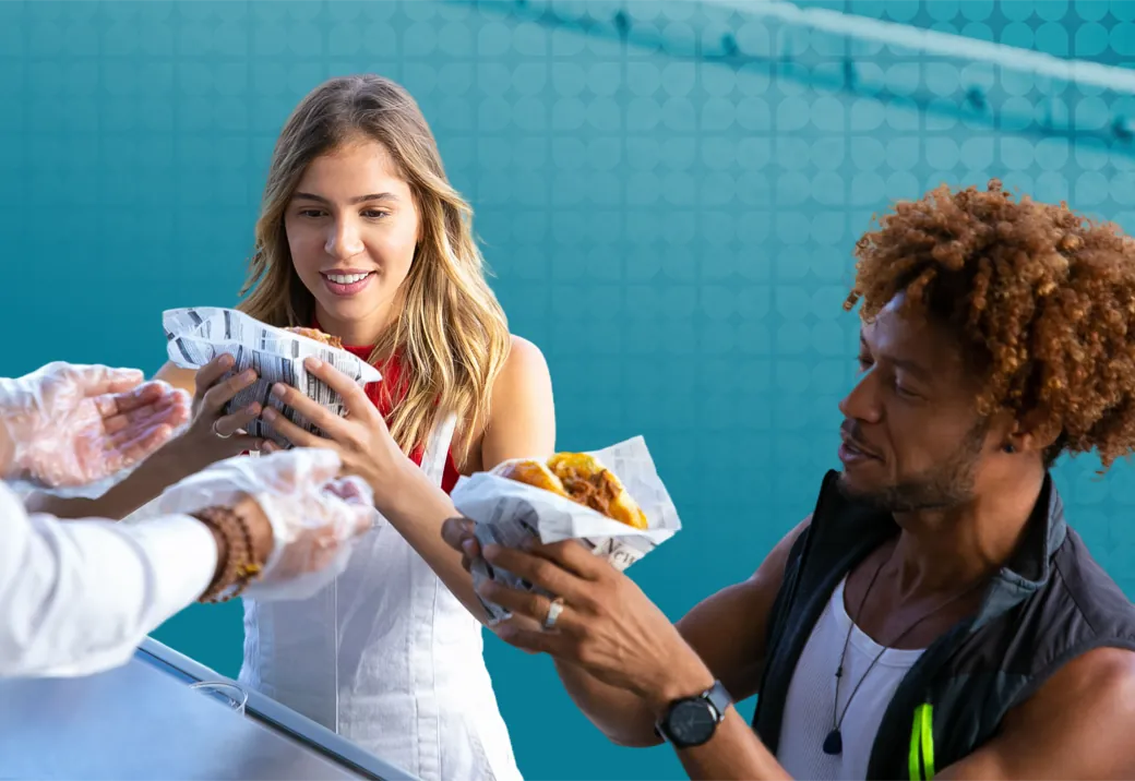 Quick-service workers handing freshly wrapped meals to two customers across the service counter