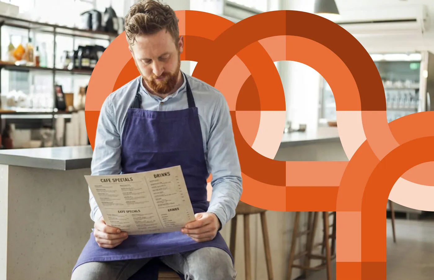 A restaurant worker in an apron reading a menu at a counter amid orange circular brand graphics
