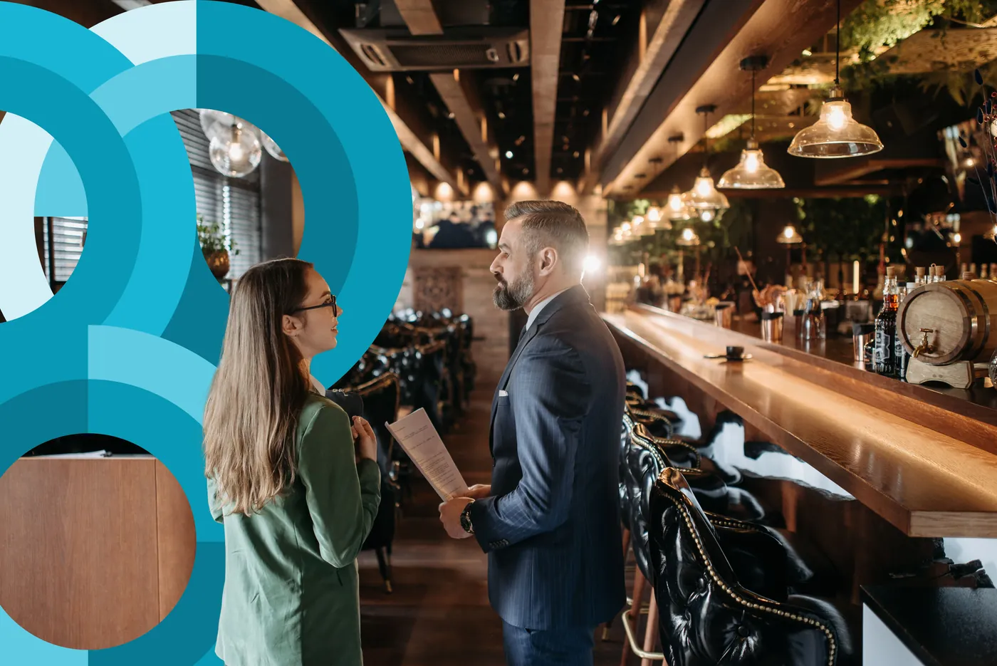 A regional manager talking with a store associate at a restaurant bar amid teal circular brand graphics