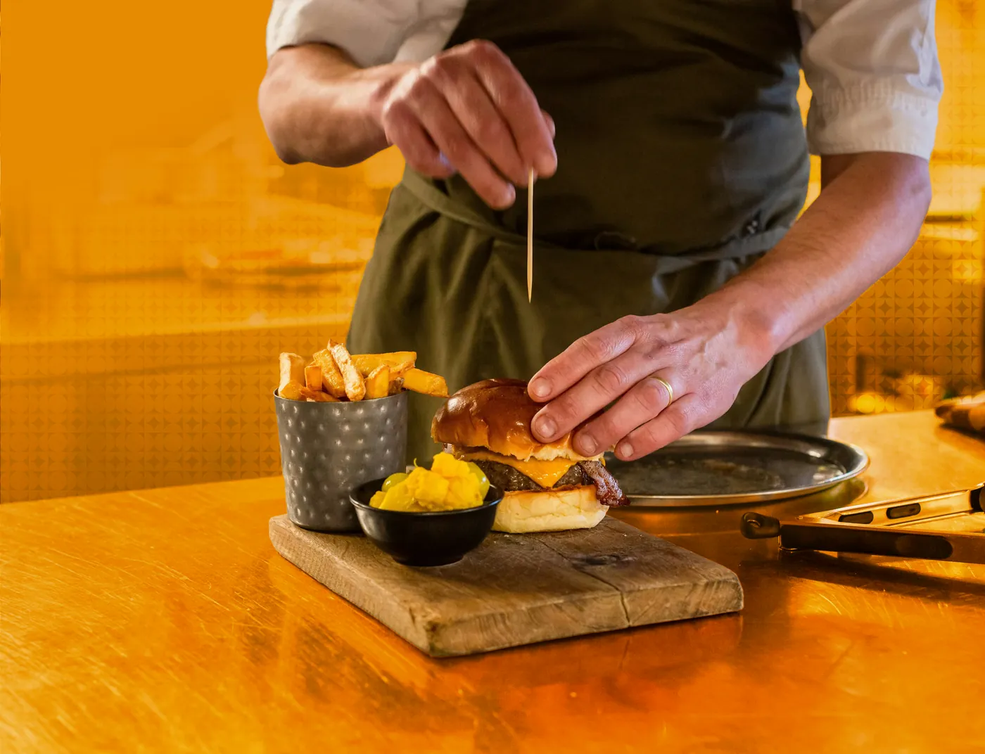 A cook plating a burger and fries on a wooden board, in amber duotone