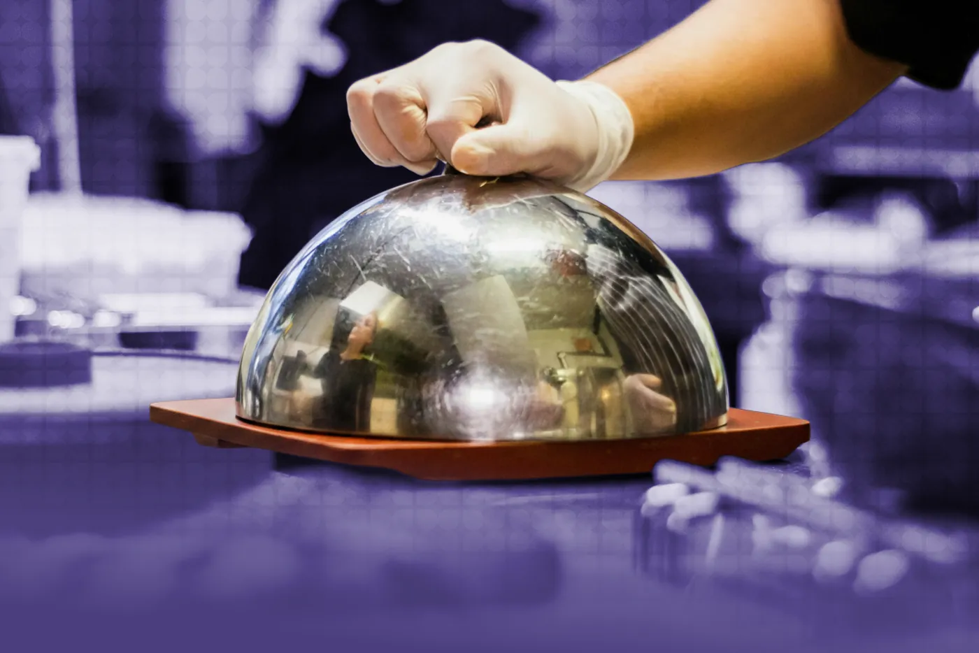 A gloved hand lifting a cloche over a plated dish, in purple duotone