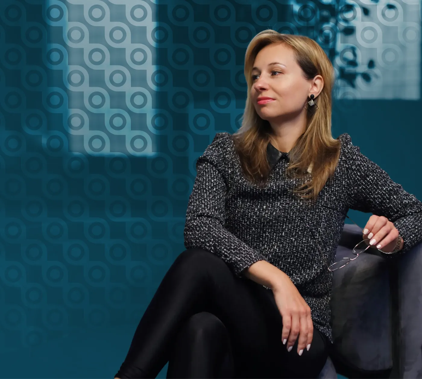 A corporate leader seated in conversation against a teal circular brand-pattern backdrop