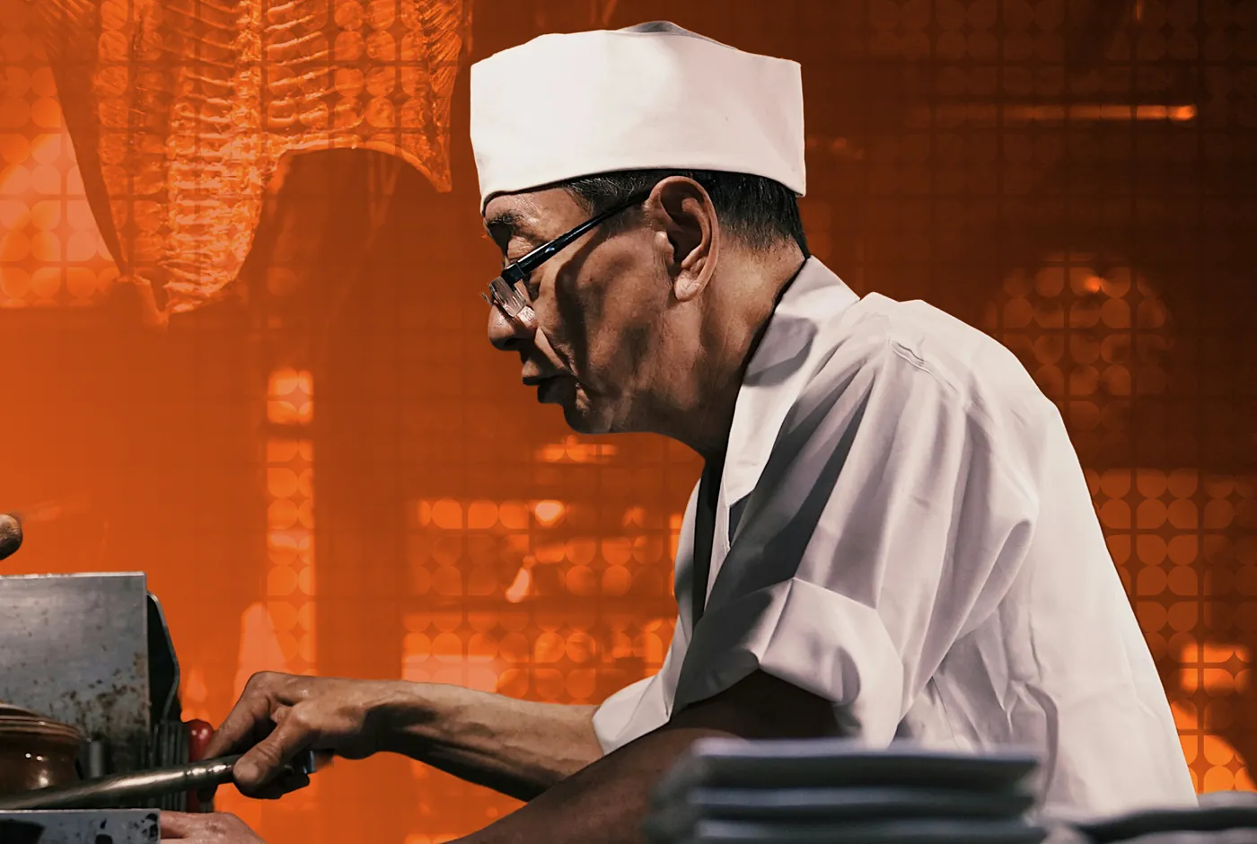 A sushi chef preparing rolls at a counter, in orange duotone