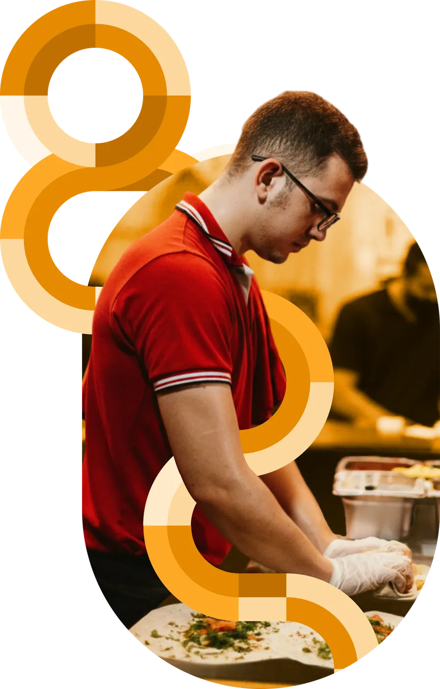 A deli worker in a red polo preparing food at a counter amid orange circular brand graphics