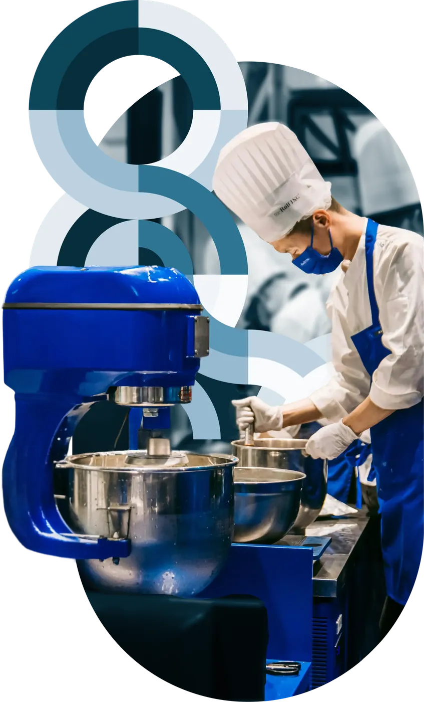 A commercial stand mixer in front of a chef working a prep station amid blue circular brand graphics