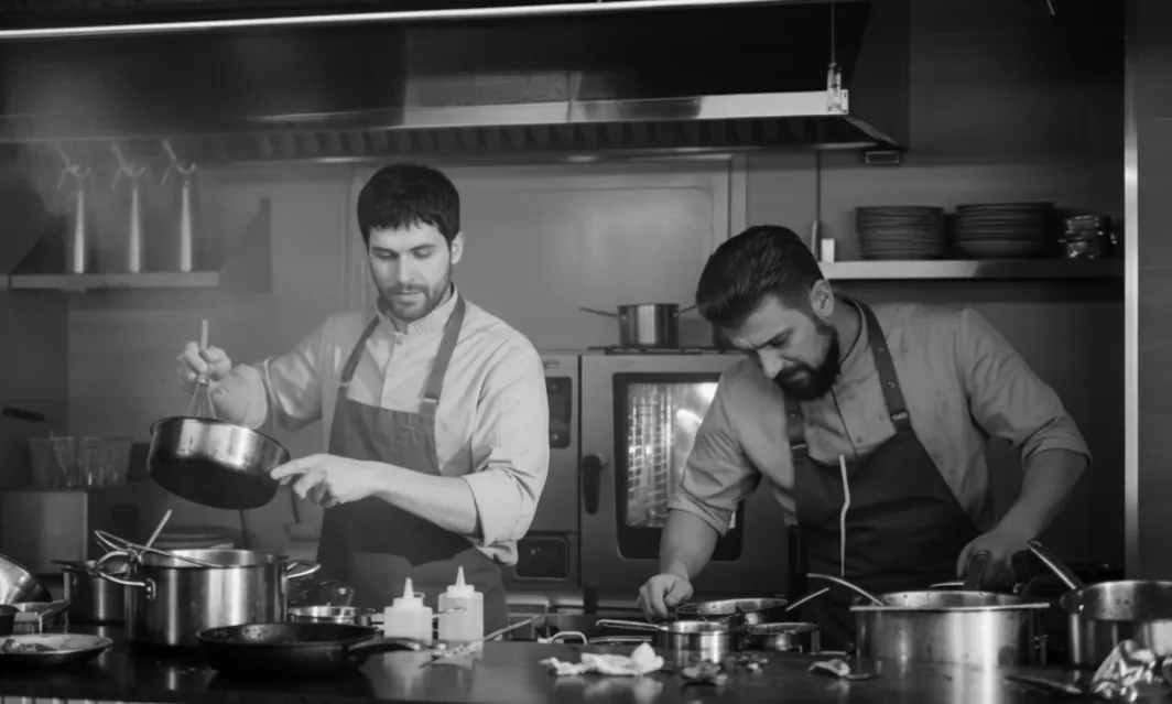Two cooks working a back-of-house kitchen line, in black and white