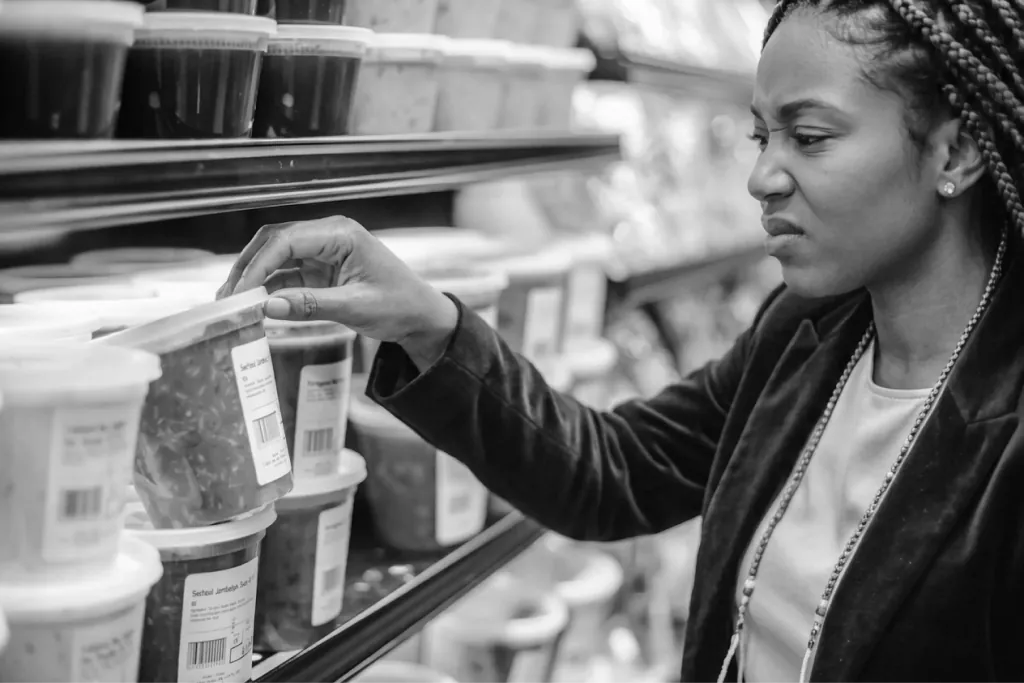 A shopper reaching for a packaged item on a convenience-store shelf, in black and white