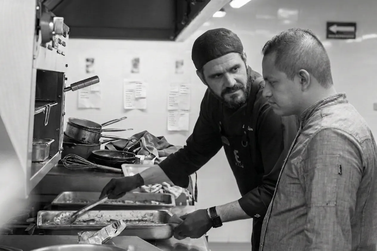 Two kitchen team members working a busy back-of-house line, in black and white