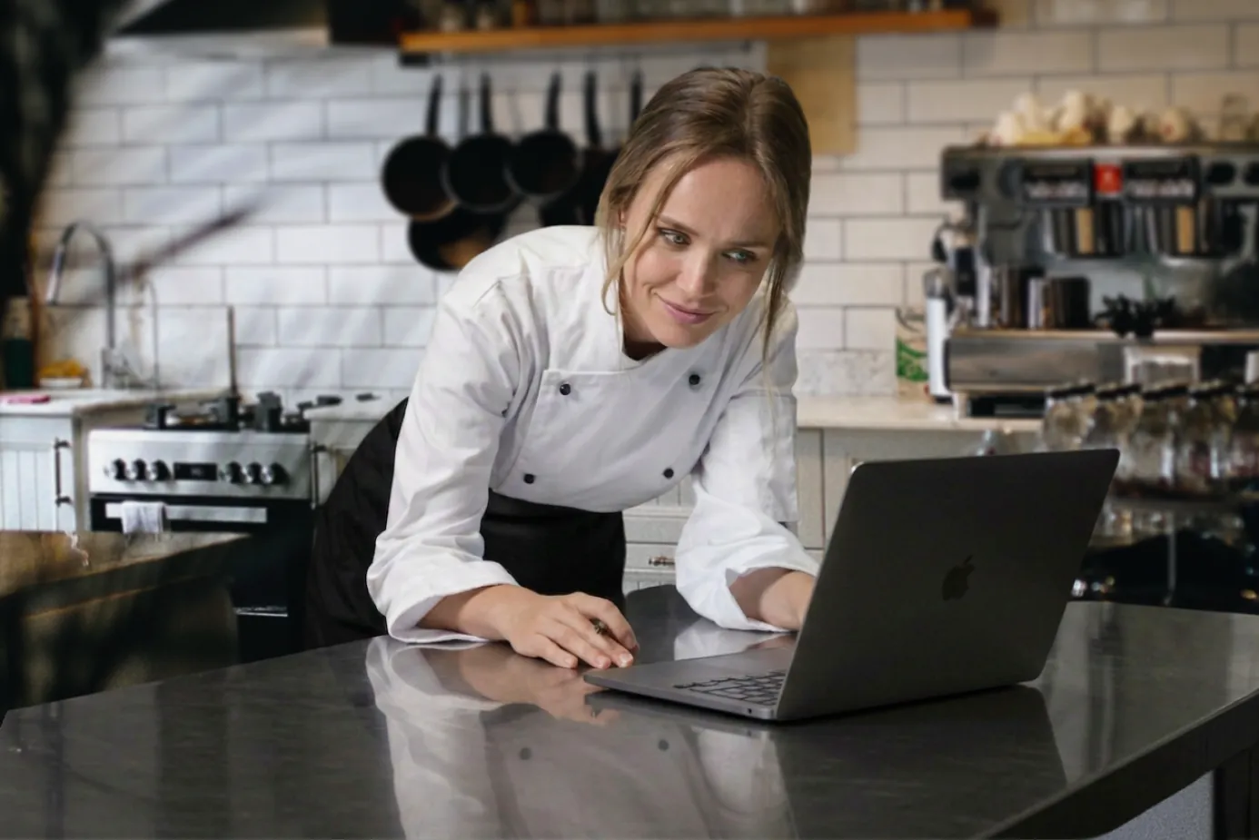 A chef reviewing records on a laptop at a kitchen prep counter