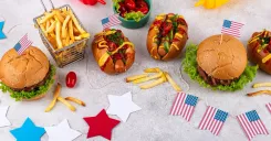 Fourth of July spread with burgers, hot dogs, fries, condiments, and American flags celebrating foodservice in America.