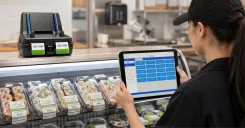 Foodservice employee using the detachable BOHA! WorkStation tablet beside a grab-and-go sushi display while the WorkStation printer base prints labels nearby.