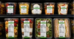 Fresh grab-and-go food items in a refrigerated display cooler with clear printed labels for prepared dates, use-by times, nutrition facts, and product information.
