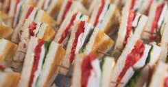 Rows of toasted chicken, tomato, and leafy green sandwiches prepared for a large catering order.