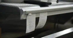 Paper tickets hanging in a restaurant back-of-house area, showing manual foodservice workflows that can become harder to manage under operational pressure.