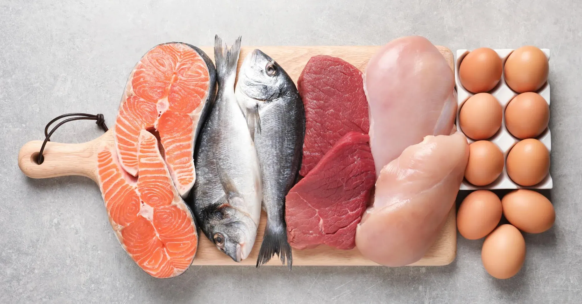 Raw salmon, whole fish, beef, chicken breasts, and eggs arranged on a cutting board as examples of TCS foods.